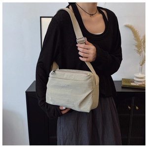Model side view of a beige nylon crossbody bag with wide strap in an indoor home setting