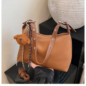 Détail d'un sac à bandoulière marron avec un joli porte-clés ours et une sangle texturée