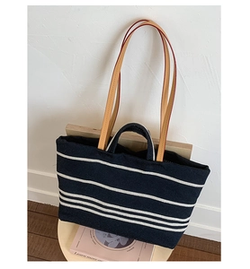 Detail view of large navy canvas tote bag with white stripes and brown leather handles