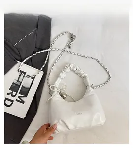 Detail of white pleated handbag with pearl bow charm and silver chain strap details