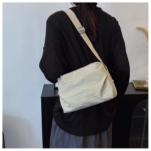 Detail of a beige nylon crossbody bag featuring adjustable straps and silver metal buckles