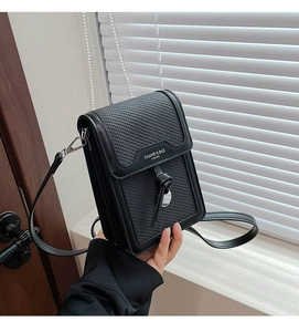 Detail view of the black vertical crossbody bag with woven texture and metal plate logo