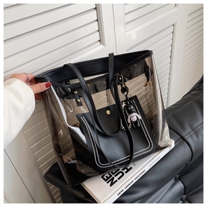 Détail d'un cabas transparent en PVC avec bordure en cuir noir et breloque ours mignon