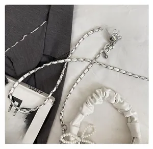 Detail of silver chain strap and pearl bow on a white pleated crossbody bag