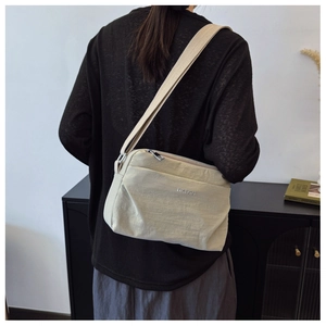 Detailed view of beige waterproof nylon crossbody bag showing broad strap and logo