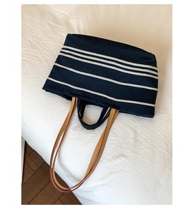 Close-up of a large striped canvas tote bag with brown shoulder straps and blue-white pattern