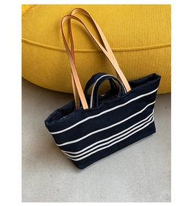 Close-up of a striped canvas tote bag with dual leather handles on a yellow sofa