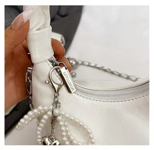 Detail of white pleated handbag featuring silver zipper, pearl chain and heart pendant