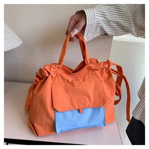 Détail du cabas en nylon orange montrant la poche bleue avant et le cordon de serrage