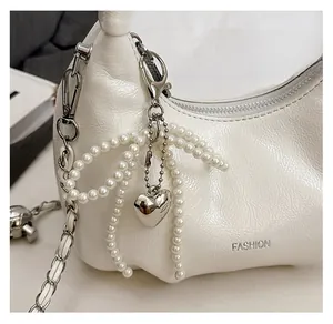 Detailed shot of a white pearl bow charm with a silver heart pendant on a leather bag