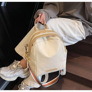 Detail of minimalist beige nylon backpack featuring a branded logo and colorful webbing strap