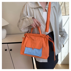 Détail du sac cabas en nylon orange avec poche bleue contrastée porté par un mannequin