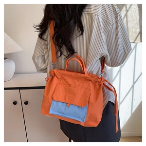 Modèle portant un sac cabas en nylon orange avec poche bleue dans un intérieur chaleureux