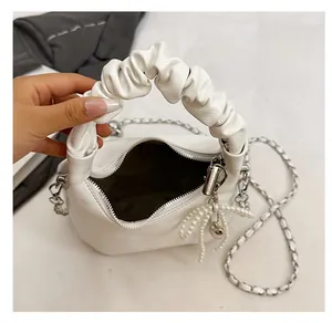 Detail view of white pleated handbag with pearl bow charm and metal chain strap