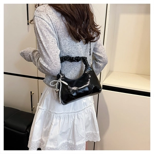 Detail of ruched handle and black patent leather moon bag with pearl bow charm