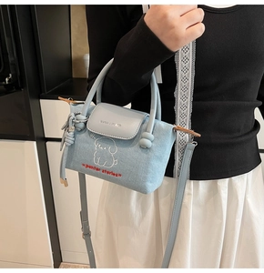 Detail of denim mini bag featuring cartoon dog embroidery and adjustable leather strap