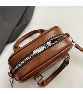 Detail of vintage brown leather handbag featuring a smooth zipper and silver metal strap hook