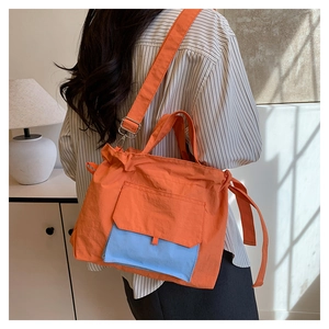 Détail du sac fourre-tout en nylon orange avec poche bleue porté en décor décontracté