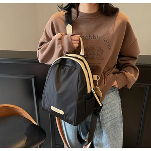 Detail view of small black nylon backpack featuring beige leather trim and side pockets