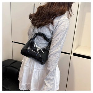 Detail of a black shiny bag with a scrunchie handle and a pearl bow charm decoration