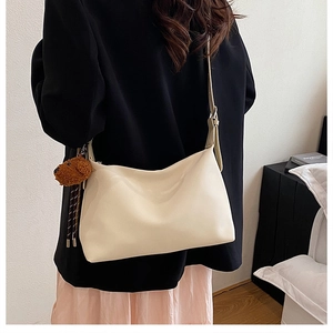 Sac bandoulière blanc cassé avec breloque chien porté à l'épaule dans un décor moderne