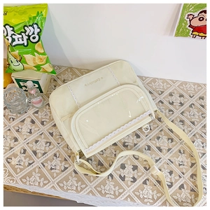 Detail of cream messenger bag showing clear PVC pocket with lace trim and mesh side