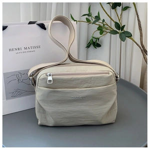 Detail of a beige nylon crossbody bag with zipper pockets and adjustable shoulder strap