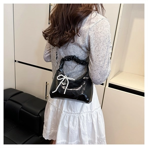 Detailed view of black patent leather hobo bag with pearl bow and heart charm on a model