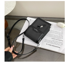 Close-up of black woven leather mini crossbody bag with silver logo on magazine background
