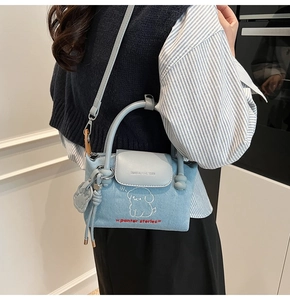 Detail shot of light blue denim mini bag featuring cartoon dog embroidery and rabbit charm
