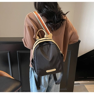 Detail of nylon backpack with beige leather trim and striped shoulder strap on model