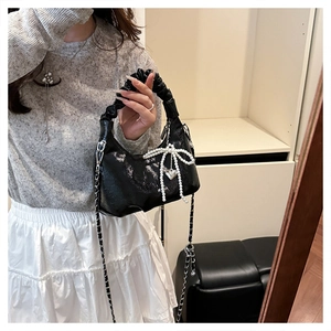 Detail of black patent leather bag with pearl bow, heart pendant, and chain strap