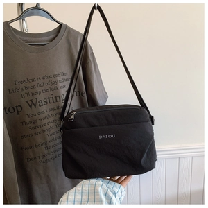 Detail of black nylon crossbody bag featuring white logo and zip closure pockets