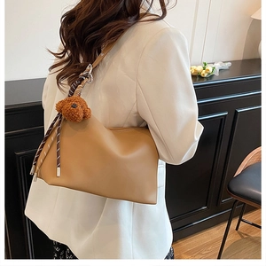 Détail d'un sac bandoulière en cuir kaki avec charm peluche sur un blazer blanc