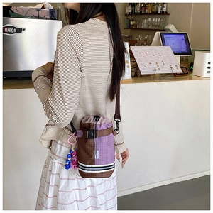 Detail of checkered bucket bag with drawstring closure and colorful charm pendant
