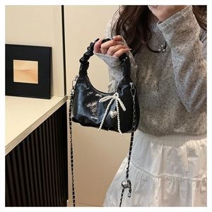 Close-up of black glossy croissant bag with pearl bow charm and chain strap detail