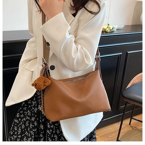 Sac hobo chic en cuir marron avec breloque ours porté sur un blazer blanc