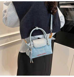 Detail of denim crossbody bag featuring puppy embroidery and leather handle on a model