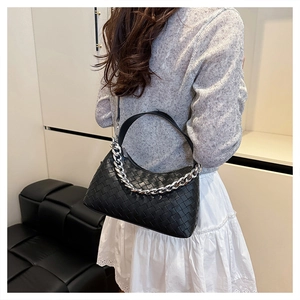 Detail of woven black leather handbag featuring a chunky silver chain and textured finish