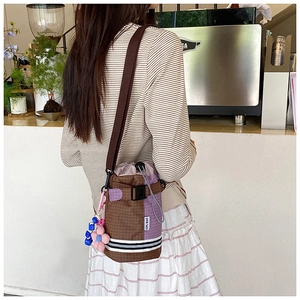 Detail of color-block plaid bicycle bucket bag with drawstring and floral charm