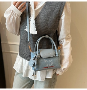 Detail of light blue denim mini bag with cartoon dog embroidery and matching charm