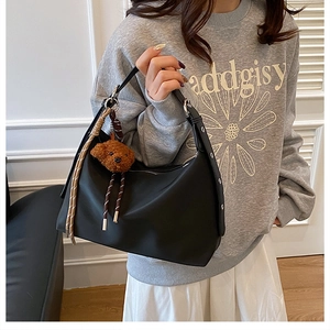 Détail du sac à bandoulière noir minimaliste avec un pendentif ours sur un modèle