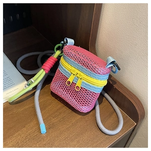 Close-up of a pink honeycomb mesh crossbody bag with yellow zippers on a wooden shelf