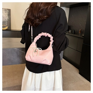 Pink pleated handbag with pearl bow and heart charm worn in a modern lifestyle setting