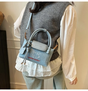 Detail of light blue denim bag featuring white dog embroidery and grey leather flap
