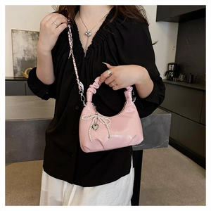 Detailed shot of pink glossy crossbody bag with pearl bow and heart metal pendant