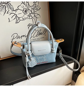 Detail of light blue denim handbag with cartoon dog embroidery and leather strap