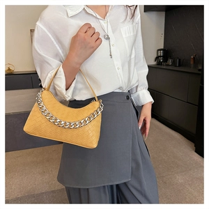 Detail of yellow woven crescent bag with silver chain worn by a model in a modern setting