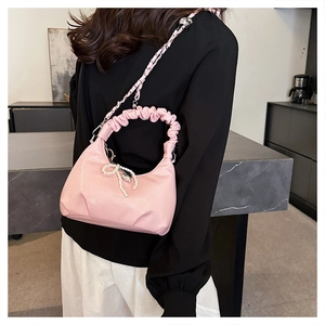 Detail of pink dumpling bag showing ruffled handle and pearl bow charm with chain strap