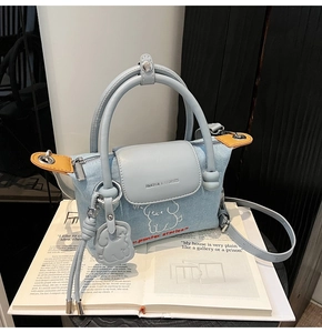 Detail of light blue denim handbag with white cartoon embroidery and yellow leather trim